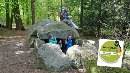 Wanderer beim Großsteingrab Steinfelder Holz mit Qualitätsweg-Logo Wanderer beim Großsteingrab Steinfelder Holz mit Qualitätsweg-Logo