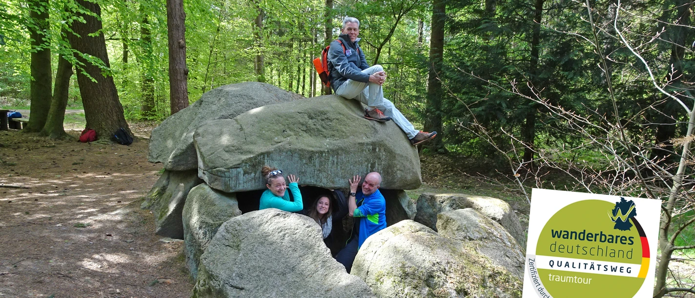 Wanderer beim Großsteingrab Steinfelder Holz mit Qualitätsweg-Logo Wanderer beim Großsteingrab Steinfelder Holz mit Qualitätsweg-Logo