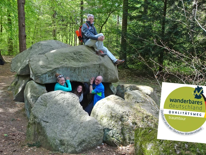 Wanderer beim Großsteingrab Steinfelder Holz mit Qualitätsweg-Logo Wanderer beim Großsteingrab Steinfelder Holz mit Qualitätsweg-LogoHikers at the Steinfelder Holz megalithic tomb with the quality trail logoVandrere ved megalitgraven Steinfelder Holz med kvalitetsstiens logoWandelaars bij de megalithische graftombe Steinfelder Holz met het logo van het kwaliteitspad