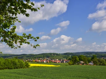 Schöne Aussichten Landschaft mit weitem Feld, gelbem Raps und einem Dorf im Grünen unter blauem Himmel.