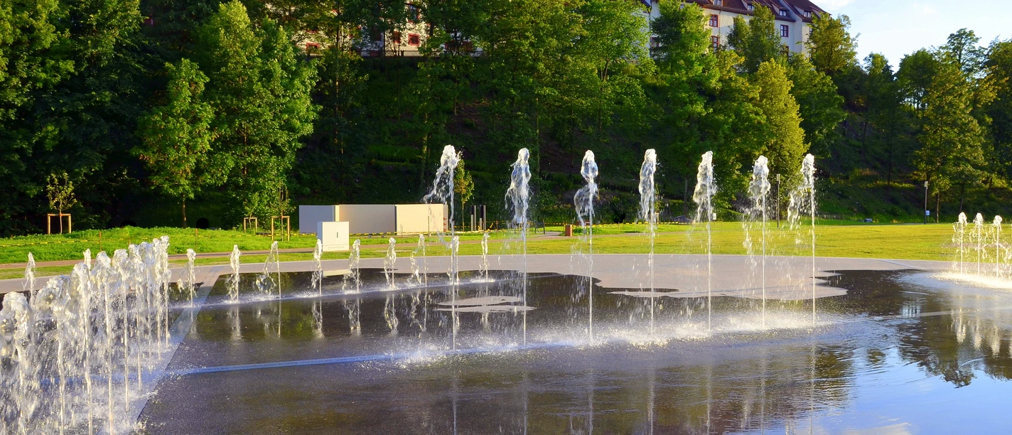 Fontein voor een ruim, historisch gebouw met een rood dak en een groene omgeving.