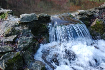 Kleine waterval stroomt over rotsen in een rustige vijver.