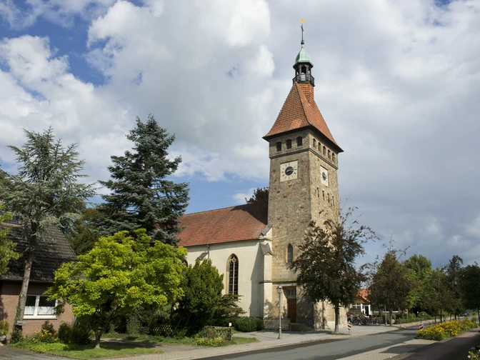 Eine historische Kirche mit hohem Turm und rotem Dach, umgeben von grünen Pflanzen und Bäumen.