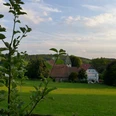 Blick auf eine Kirche und Fachwerkhäuser hinter grünen Feldern und Bäumen unter blauem Himmel.View of a church and half-timbered houses behind green fields and trees under a blue sky.Udsigt til en kirke og bindingsværkshuse bag grønne marker og træer under en blå himmel.Zicht op een kerk en vakwerkhuizen achter groene velden en bomen onder een blauwe lucht.