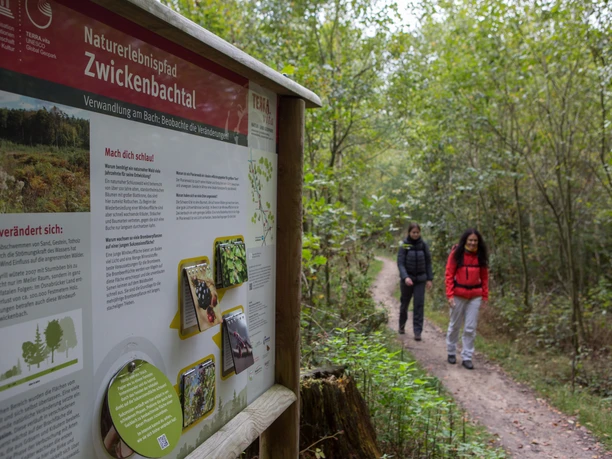Bewegwijzerde wandelroute door de Zwickelbachvallei op het platteland, twee wandelaars op de achtergrond.