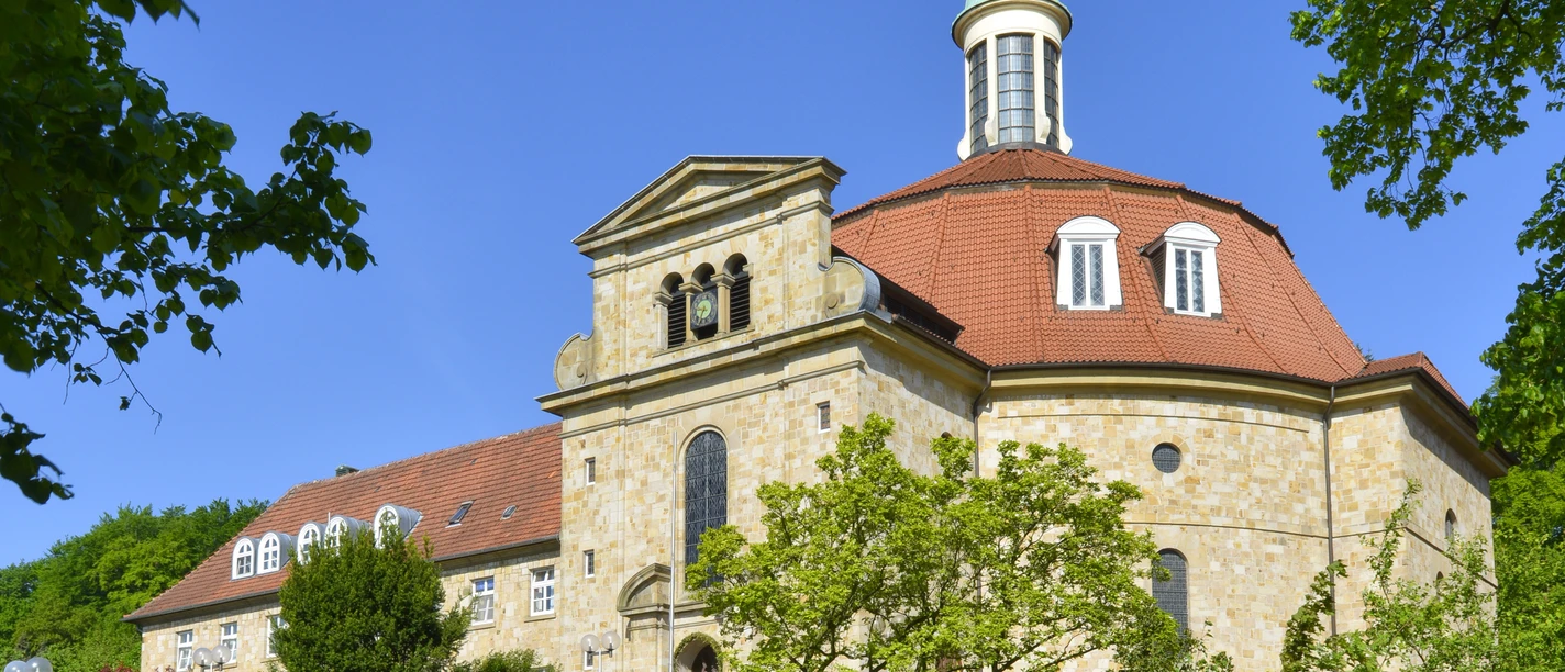Kloster Ohrbeck Church with octagonal tower, blue dome and stone wall on a sunny, clear day.