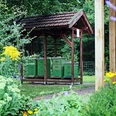 lehrbienenstand Grüne Bienenstöcke unter einem Holzunterstand, umgeben von farbenfrohen Blumen.
