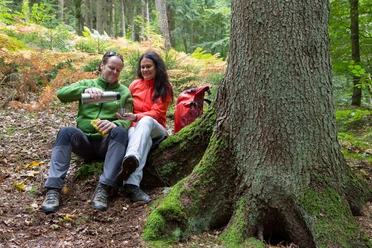 Pause am Wegesrand A couple in outdoor outfits enjoy a break in the forest and pour tea into a mug.
