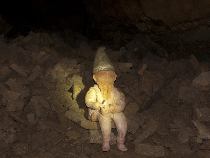 Ein Zwerg mit Spitzhut sitzt auf Steinbrocken in einer dunklen Höhle.A dwarf with a pointed hat sits on boulders in a dark cave.En dværg med en spids hat sidder på sten i en mørk hule.Een dwerg met een puntmuts zit op rotsblokken in een donkere grot.