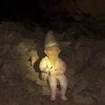 Ein Hüggelzwerg Ein Zwerg mit Spitzhut sitzt auf Steinbrocken in einer dunklen Höhle.