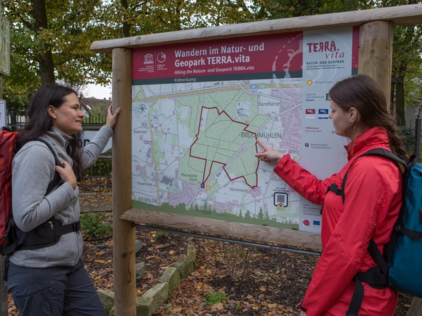 Twee wandelaars bekijken een kaart van het TERRA.vita Natuur- en Geopark in het bos.