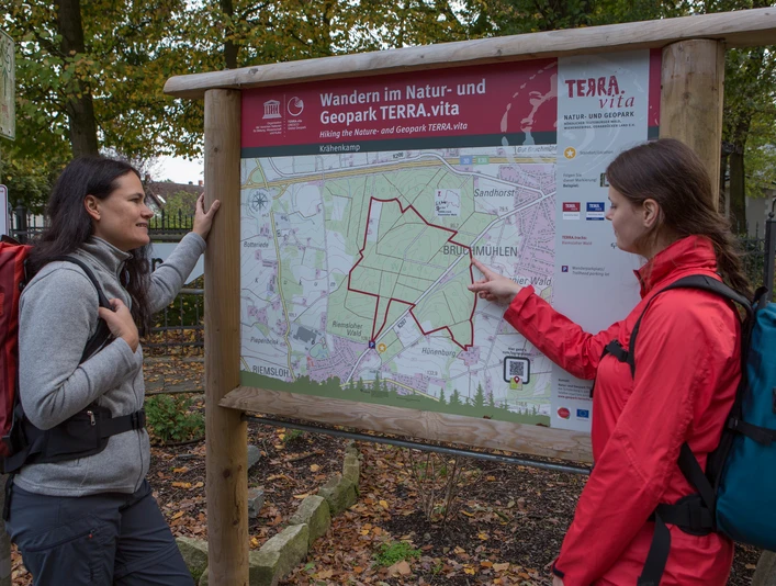 Wandertafel TERRA.vita Zwei Wanderer betrachten eine Karte des Natur- und Geoparks TERRA.vita im Wald.Two hikers look at a map of the TERRA.vita Nature and Geopark in the forest.To vandrere kigger på et kort over TERRA.vita Nature and Geopark i skoven.Twee wandelaars bekijken een kaart van het TERRA.vita Natuur- en Geopark in het bos.