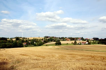 Blick auf Hummerbruch Blick auf goldene Getreidefelder im Vordergrund mit einer kleinen, von Windrädern umrahmten Ortschaft.