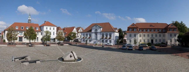 Panorama Marktplatz Quakenbrück.jpg Weitläufiger Platz mit Kopfsteinpflaster, modernen Skulpturen und historischen Gebäuden.