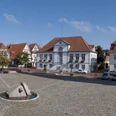 Panorama Marktplatz Quakenbrück.jpg Weitläufiger Platz mit Kopfsteinpflaster, modernen Skulpturen und historischen Gebäuden.