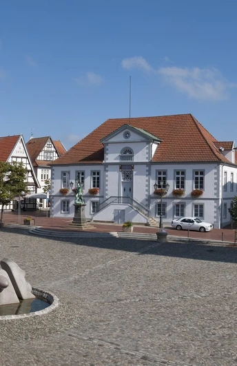 Panorama Marktplatz Quakenbrück.jpg Weitläufiger Platz mit Kopfsteinpflaster, modernen Skulpturen und historischen Gebäuden.