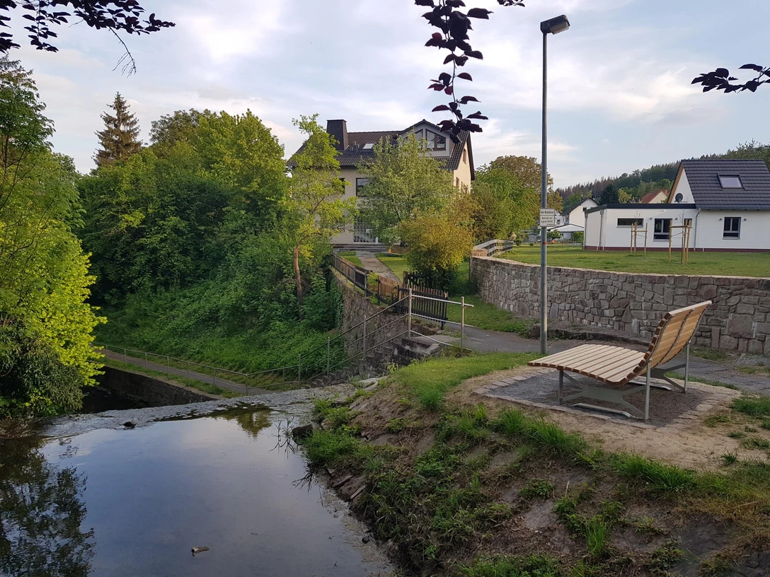Landschaftsliege an kleinem treppenförmigen Wassertreppe an der Saumer, Gärten und Wohnhäuser im Hintergrund