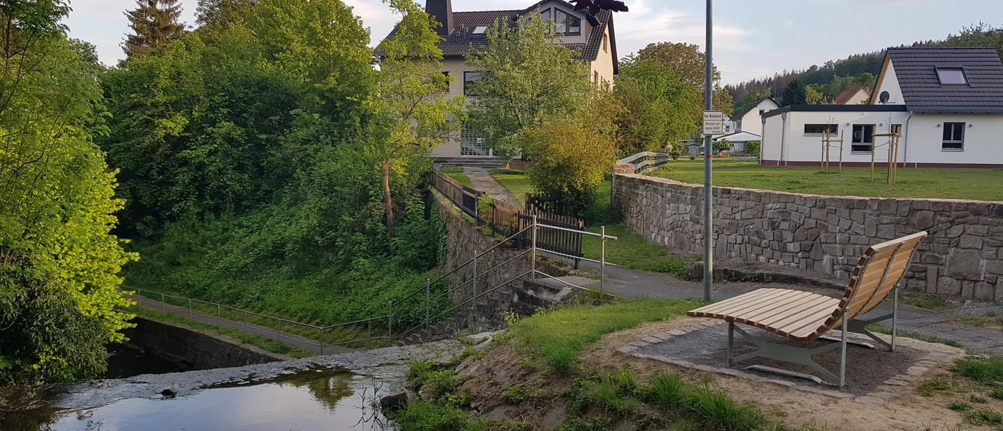 Landschaftsliege an kleinem treppenförmigen Wassertreppe an der Saumer, Gärten und Wohnhäuser im Hintergrund