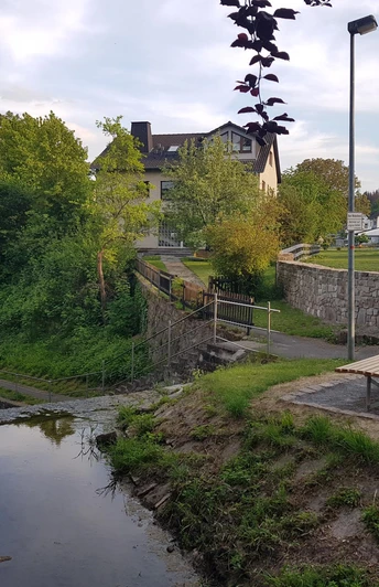 Landschaftsliege an kleinem treppenförmigen Wassertreppe an der Saumer, Gärten und Wohnhäuser im Hintergrund