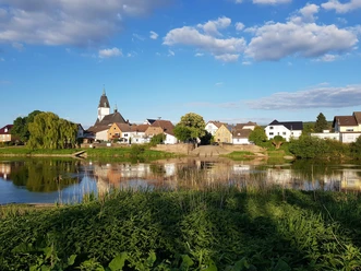 Blick auf das malerische Lüchtringen mit Kirche, Fachwerkhäusern und der Weser im Vordergrund.