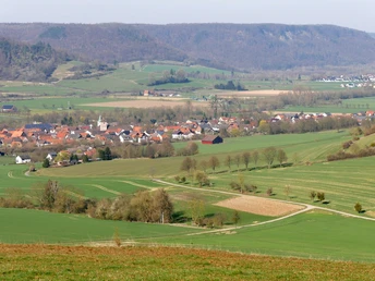 Hügelige Landschaft mit Blick auf das Dorf Amelunxen, Felder und Wälder im Hintergrund.