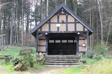 Schutzhütte auf dem Heiligenberg Waldbrauereiunterstand aus Holz und Ziegeln, umgeben von hohen Bäumen, mit hölzernem Zugang.