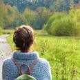 Person mit Rucksack blickt auf herbstlichen Waldweg und grüne, bewaldete Landschaft.A person with a rucksack looks out over an autumnal forest path and a green, wooded landscape.En person med en rygsæk kigger ud over en efterårsagtig skovsti og et grønt, skovklædt landskab.Een persoon met een rugzak kijkt uit over een herfstig bospad en een groen, bebost landschap.