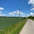 Ländliche Straße neben einem weiten Feld mit Windkraftanlagen unter blauem Himmel und Wolken.