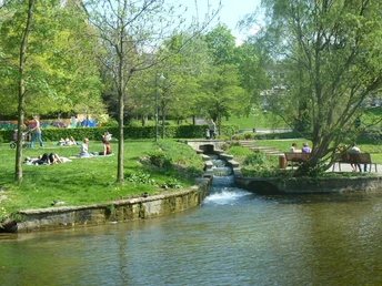 Grünes Stadtareal mit Bachlauf, Wiesen und Spaziergängern im westlichen Paderquellgebiet.