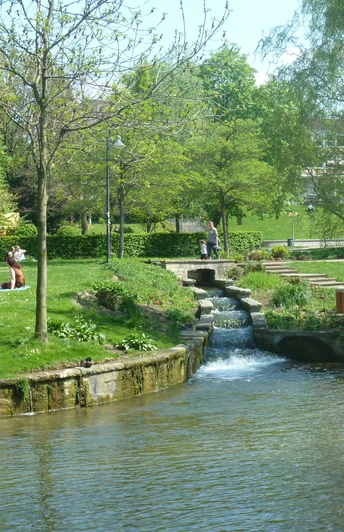 Grünes Stadtareal mit Bachlauf, Wiesen und Spaziergängern im westlichen Paderquellgebiet.