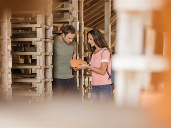 lage-ziegeleimuseum-teutoburger-wald-tourismus-m-schoberer-1 Ein Paar betrachtet interessiert einen Ziegelstein in einem traditionellen Handwerksbetrieb.