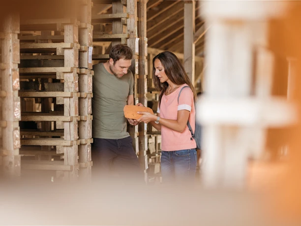 lage-ziegeleimuseum-teutoburger-wald-tourismus-m-schoberer-1 Ein Paar betrachtet interessiert einen Ziegelstein in einem traditionellen Handwerksbetrieb.