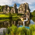Yoga vor den Externsteinen Eine Person praktiziert Yoga auf einer Plattform vor den majestätischen Externsteinen in einer grünen Umgebung.