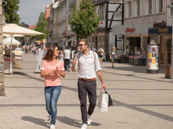 detmold-innenstadt-teutoburger-wald-tourismus-m-schoberer Zwei Menschen spazieren lächelnd durch eine belebte Fußgängerzone, beide mit Eis in der Hand.