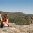 detmold-ruine-falkenburg-teutoburger-wald-tourismus-m-schoberer-4 Zwei Menschen genießen von einer Mauer am Berg aus den Blick auf die bewaldete Landschaft.