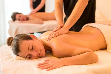Entspannende Massage im H2O Herford Zwei Personen genießen entspannende Rückenmassagen auf Massageliegen in einem Wellnessbereich.