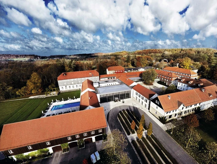 Gräflicher Park Health & Balance Resort mit roten Dächern, umgeben von herbstlichen Bäumen und Rasenflächen.