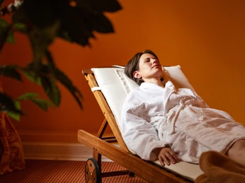 Eine Frau ruht in einem Bademantel auf einer Holzliege im Gräflichen Park Health & Balance Resort.
