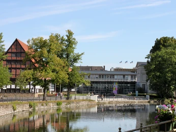 Lippisches Landesmuseum Detmold Historisches Fachwerkgebäude neben modernem Museumsbau am Wasser, umgeben von grünen Bäumen.
