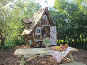 Hexenhäuschen Kleines, schiefwinkeliges Häuschen im Wald mit Picknicktisch im Vordergrund und blühenden Pflanzen.