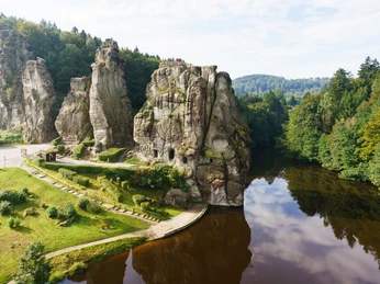 Historische Sandsteinfelsen im Teutoburger Wald, umgeben von dichten Wäldern und einem ruhigen See.