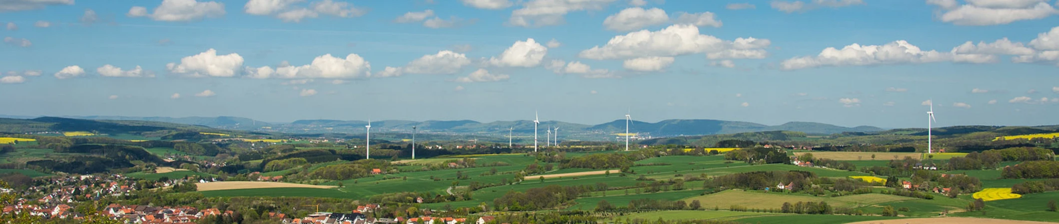 Panoramablick über eine weitläufige grüne Landschaft mit Windrädern und kleinen Siedlungen.