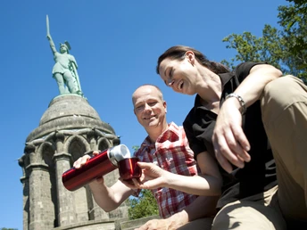 Am Hermannsdenkmal Ein Paar sitzt vor dem Hermannsdenkmal und genießt eine Pause bei strahlend blauem Himmel.