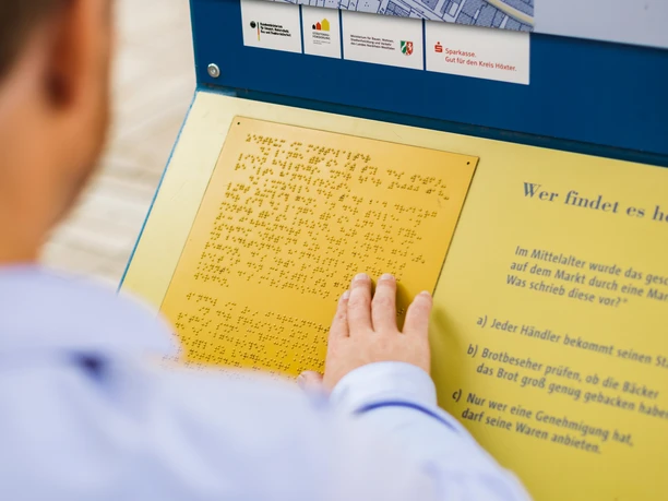 Informationstafel am barrierefreien Stadtrundgang Informationstafel mit Brailleschrift und Stadtkarte, die Teil eines barrierefreien Stadtrundgangs ist.