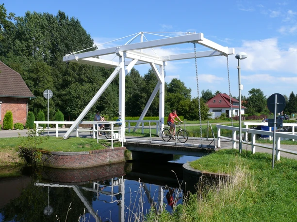 Klappbrücke in Ostrhauderfehn Die weiße Klappbrücke in Ostrhauderfehn überspannt einen kleinen Kanal, während Menschen auf Fahr- und Motorrädern sie überqueren.