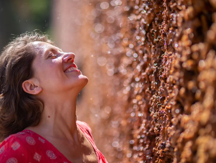 Tief durchatmen Eine lächelnde Frau genießt die salzhaltige Luft an einer Gradierwand, umgeben von Sonnenlichtern.