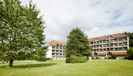 Außenansicht Hotel Bärenstein Hotel Bärenstein mit rotem Dach, großen Fenstern und grüner Wiese im Vordergrund unter bewölktem Himmel.