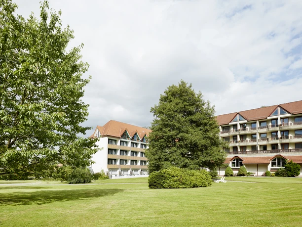 Außenansicht Hotel Bärenstein Hotel Bärenstein mit rotem Dach, großen Fenstern und grüner Wiese im Vordergrund unter bewölktem Himmel.