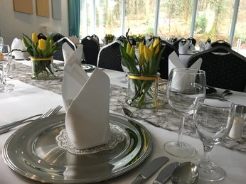 Restaurant Elegant gedeckter Tisch mit silbernem Teller, Stoffserviette, Weingläser und gelben Tulpenarrangements.