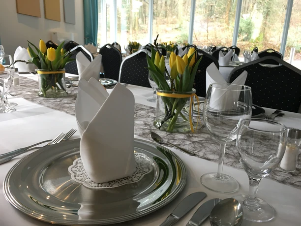 Restaurant Elegant gedeckter Tisch mit silbernem Teller, Stoffserviette, Weingläser und gelben Tulpenarrangements.